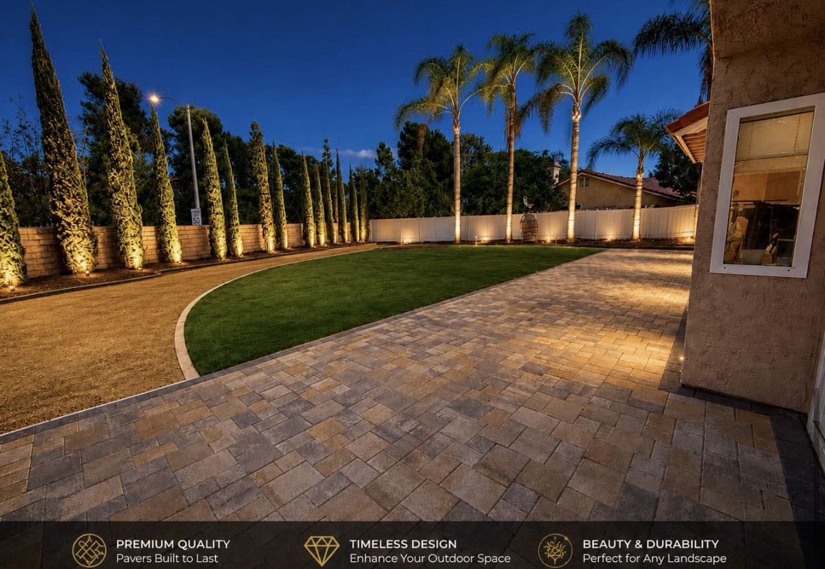 Illuminated landscaped backyard with pavers and turf